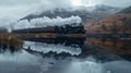 A steam engine train driving along the lake in the valley with its reflection on the water