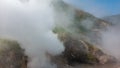 Steam from the erupting geyser envelops the slope of the hill.