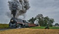 Steam Frieght Train Passing an Antique Tractor with Black Smoke and Steam