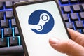 Steam logo on a phone screen with a blue gaming keyboard background. app for pc games platform icon on smartphone display. Italy,