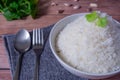 Steam organic white rice in white ceramic bowl with silver cutlery and apron and green coriander stained on a brown wooden table