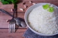 Steam organic white rice in a white ceramic bowl with silver cutlery and apron and green coriander stained on a brown wooden table