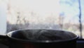 Steam rises while cooking in a pan. Open a small pan with steam. The stewpan stands on the windowsill near the window and cools do