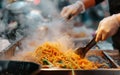 Steam rises from a sizzling wok as noodles are expertly tossed at a bustling street food market stall.