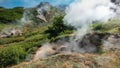 Steam and smoke rise from the fumarole on the hillside.