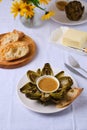 Steamed artichoke with vinaigrette sauce based on oil and mustard on a white plate on a light background. Served with fresh Royalty Free Stock Photo