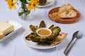 Steamed artichoke with vinaigrette sauce based on oil and mustard on a white plate on a light background. Served with fresh Royalty Free Stock Photo