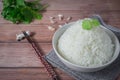 Steamed organic white rice in a white ceramic bowl with chopsticks and apron and green coriander stained on a brown wooden table