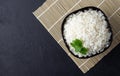 Steamed rice on black plate over bamboo tablecloth. Black stone background.