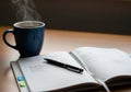 A steaming blue mug sits on a wooden surface next to an open planner with a pen placed on top. The Royalty Free Stock Photo