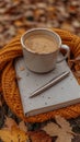 A cup of coffee on a journal with a yellow knitted scarf, surrounded by autumn leaves Royalty Free Stock Photo