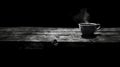 A steaming cup of coffee sits on a rustic wooden table against a stark black background