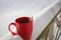 Steaming Cup of Hot Coffee or Tea standing on the Outdoor Table in Snowy Winter Morning. Cozy Festive Red Mug with a