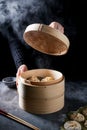 Steaming Dim Sum dumplings in a bamboo steamer. Male hands lifting the lid and steam coming out.