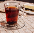 Steaming glass of black tea resting on tablecloth with cake in background Royalty Free Stock Photo