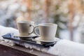 Steaming hot coffee in two mugs, buried in snow, on a balcony, on a bright winter morning. Breakfast for two. Cozy