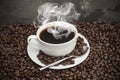 Steaming hot cup of coffee surrounded by dark coffee beans Royalty Free Stock Photo