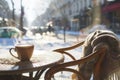 Steaming hot cup of coffee on wooden table of beautiful snow covered typical Parisian cafe in France. Sunny cold day on winter