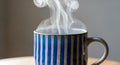 Steaming mug with blue and white vertical stripes sits on a wooden surface. The Royalty Free Stock Photo