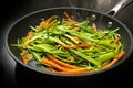 Steaming vegetable noodles from fresh carrot julienne and green leek strips in a black frying pan, cooking a healthy vegetarian