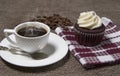 Steaming white coffee cup, homemade cupcake and coffee beans on brown fabric background, cake with cream