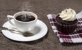 Steaming white coffee cup and homemade cupcake on brown fabric background, homemade cake