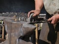 Steel anvil, on top of which lies a hot workpiece which is held by a pair of pliers, semi-circular smoothing stone in the hand