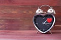 Steel clock alarm in the form of a heart, with a red heart on a pink wooden background. Valentine`s Day