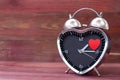 Steel clock alarm in the form of a heart, with a red heart on a pink wooden background. Valentine`s Day