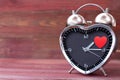 Steel clock alarm in the form of a heart, with a red heart on a pink wooden background. Valentine`s Day