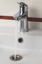 Steel faucet in the bathroom. Stream of water falling in ceramic sink. Modern metal mixer with white wash basin. Open tap. Royalty Free Stock Photo