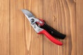 Steel gardening secateurs, scissors tool with red and black grip for pruned of plants and flowers garden work, on a wooden table