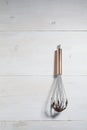 Steel hand whisk with chocolate sauce on white wooden background