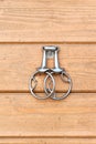 Steel horse snaffle-bit hanging on wooden background.