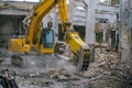 Steel hydraulic attachment pliers on excavator grappling construction debris in collapsed industrial building