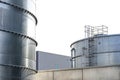 Steel industrial silos for liquids and solids standing in a factory next to a concrete building.