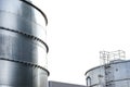 Steel industrial silos for liquids and solids standing in a factory, white sky in the background.