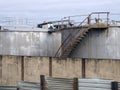 Steel industrial storage tanks with rusty stairs and walkways behind a shabby corrugated iron fence and wall Royalty Free Stock Photo