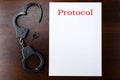 Steel police handcuffs and empty protocol list lying on wooden t Royalty Free Stock Photo