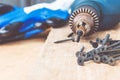 A steel screw is placed on an electric drill near scattered screws on a wooden board background. The concept of tools and repair Royalty Free Stock Photo