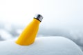 Steel thermo bottle of yellow color in snow. Close-up view. Reusable thermos