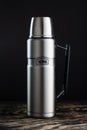 Steel Thermos flask by Termos on a wooden table against a black wall