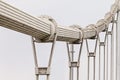 Steel thick twisted suspension bridge cable with a number of metal loops against the white sky background going into the distance