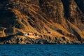 Steep cliff on the coast with small houses in stinted landscape in Norway on bright sunny day seen from boat