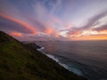 Steep green grass oceanside hill cliff with pastel sky sunset at Cape Reinga New Zealand Tasman Sea Pacific Ocean