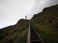 Steep wooden staircase steps leading up to red and white lighthouse on top of oceanside hill, Cape Palliser New Zealand Royalty Free Stock Photo