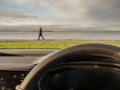 Steering wheel in focus. Nature scene with ocean, mountain and a man walking by out of focus. Travel by car concept Royalty Free Stock Photo