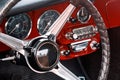 Steering wheel, speedometer, revs, clock dials, radio scale, buttons and knobs on front panel red coupe old timer sports car Royalty Free Stock Photo