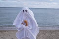 Ghost at seashore holding pumpkin on halloween
