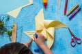 Step-by-step making of a paper weather vane by a child on a blue concrete background. Children`s creativity, divas, crafts